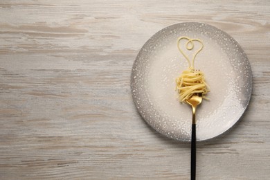 Photo of Heart made with spaghetti and fork on light wooden table, top view. Space for text