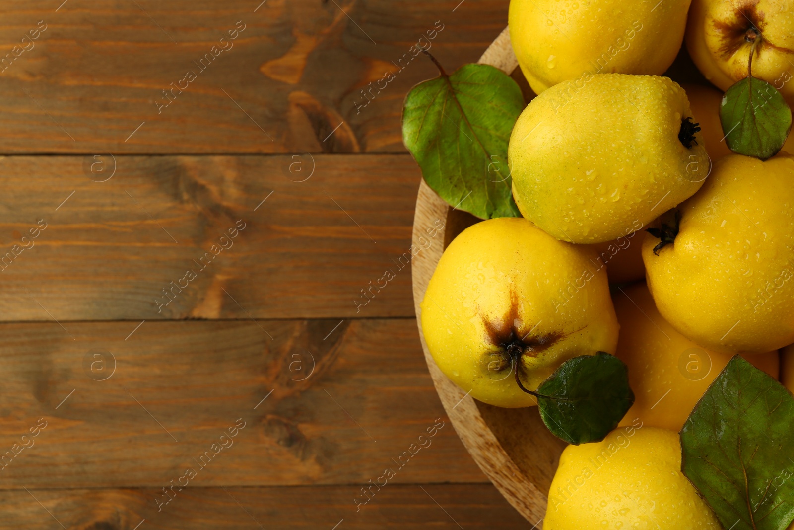 Photo of Tasty ripe quince fruits with water drops in bowl on wooden table, top view. Space for text