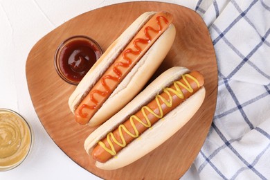 Tasty hot dogs with ketchup and mustard on white table, flat lay