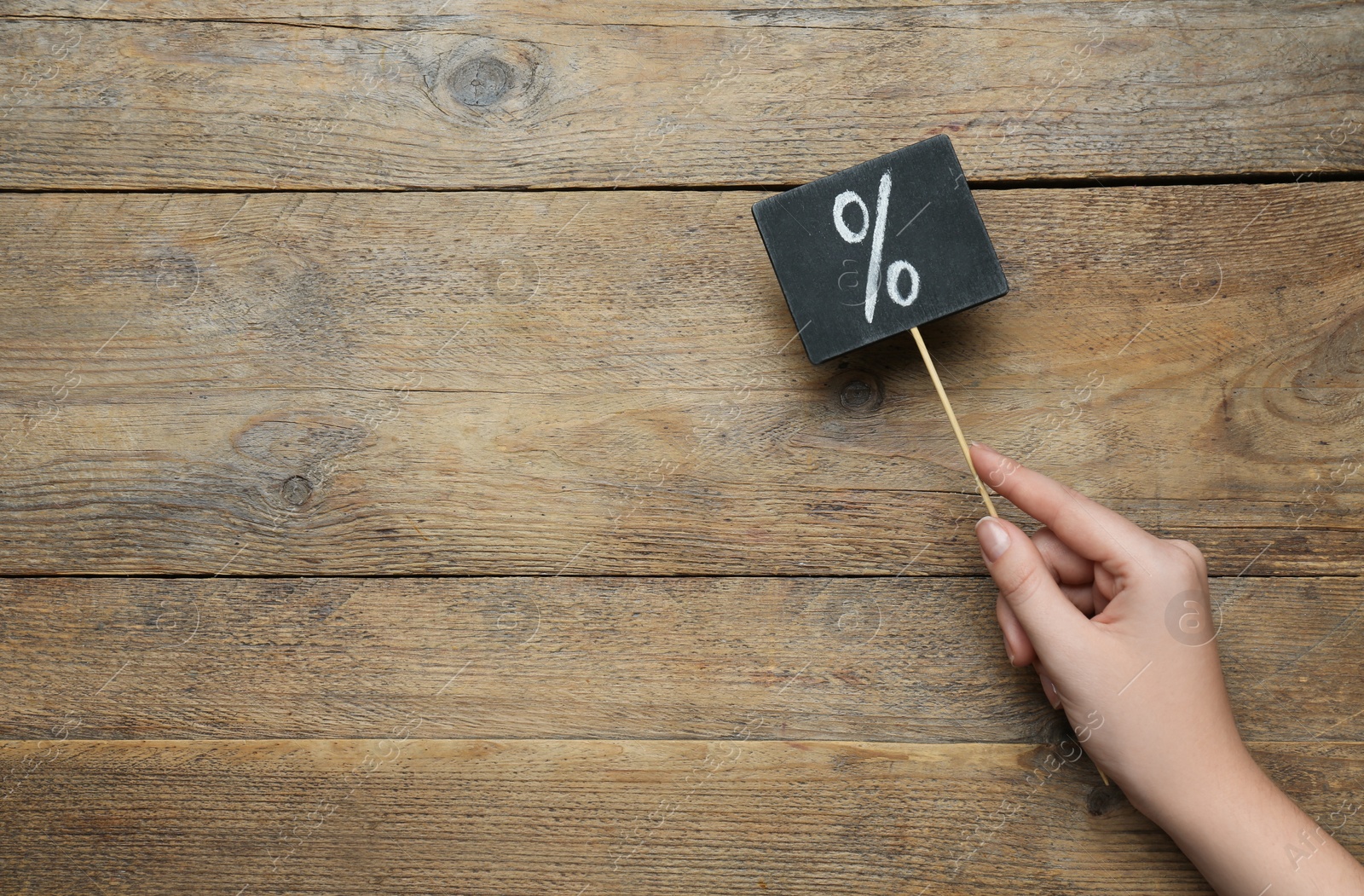 Photo of Woman holding sign with percent symbol on wooden background, top view. Space for text