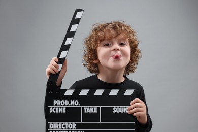 Photo of Happy cute boy with clapperboard on grey background. Little actor