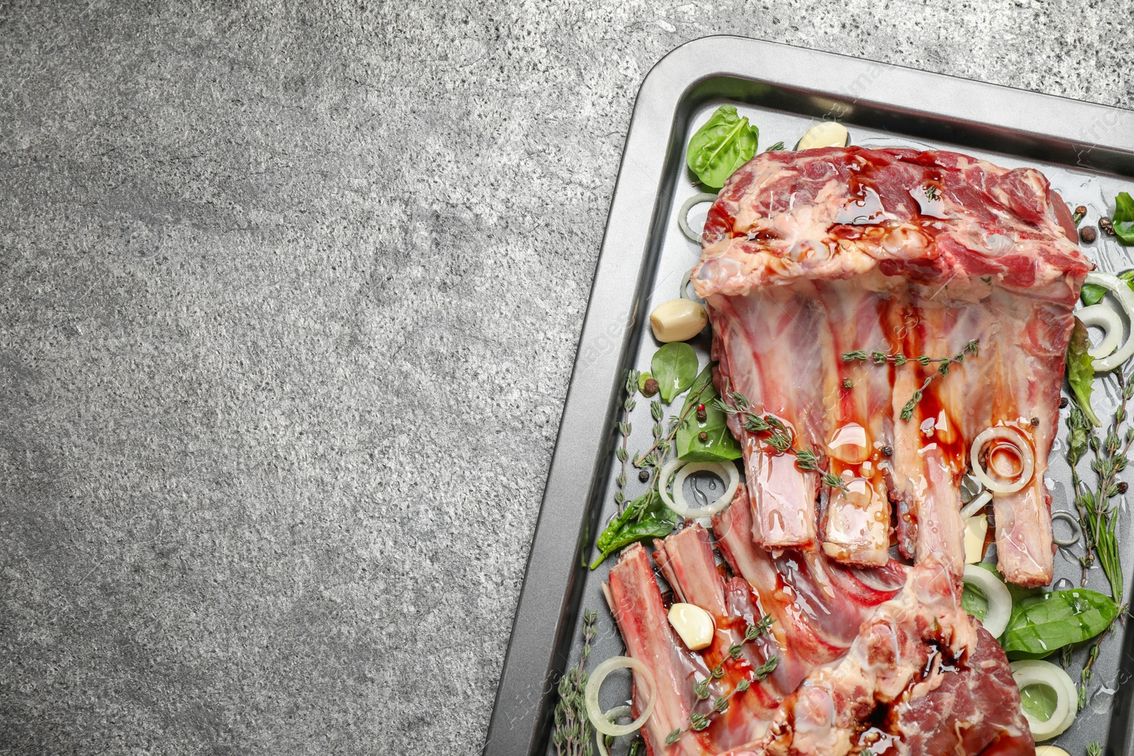 Photo of Raw spare ribs with herbs and seasonings on grey table, top view. Space for text