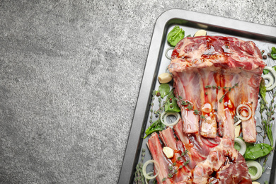 Photo of Raw spare ribs with herbs and seasonings on grey table, top view. Space for text