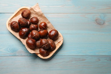 Photo of Fresh edible sweet chestnuts in serving plate on light blue wooden table, top view. Space for text