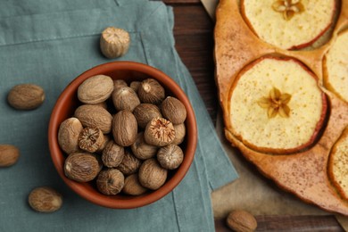 Photo of Nutmeg seeds and tasty apple pie on wooden table, flat lay