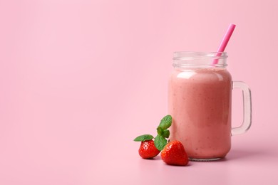 Photo of Mason jar with delicious berry smoothie and fresh strawberries on pink background. Space for text