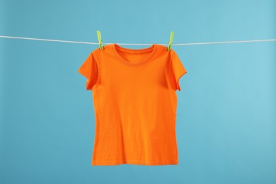 Photo of One orange t-shirt drying on washing line against light blue background