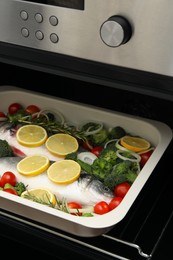 Photo of Raw fish with vegetables and lemon in baking dish into oven