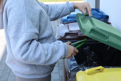 Photo of Woman throwing glass bottle in bin outdoors, closeup. Recycling concept
