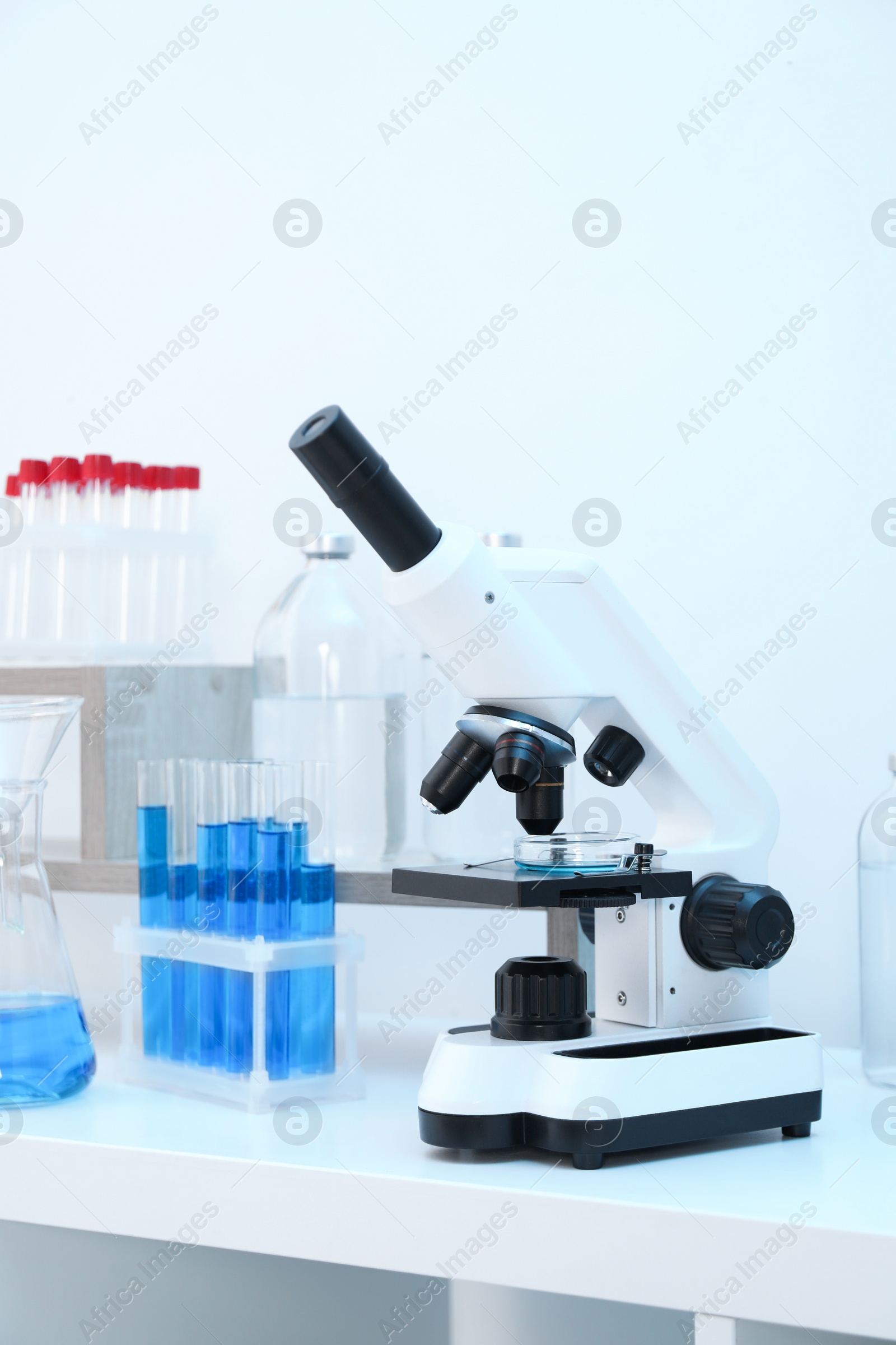 Photo of Laboratory analysis. Different glassware with blue liquid and microscope on white table indoors