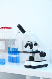 Photo of Laboratory analysis. Different glassware with blue liquid and microscope on white table indoors