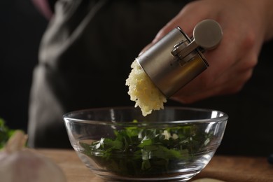 Photo of Woman squeezing garlic with press at table, closeup