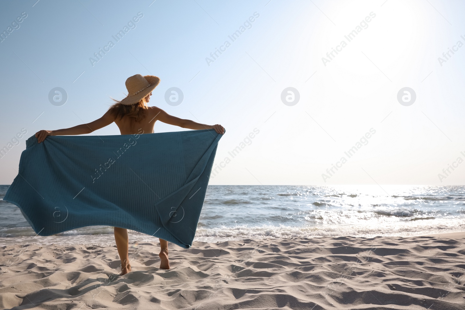 Photo of Woman with beach towel and straw hat on sand near sea, back view. Space for text