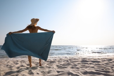Photo of Woman with beach towel and straw hat on sand near sea, back view. Space for text