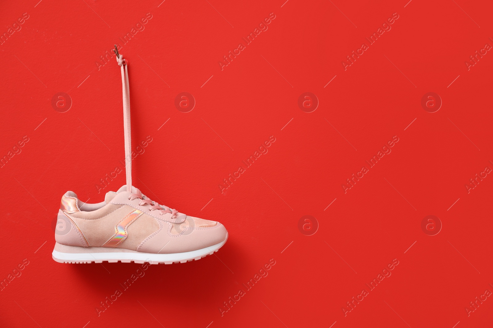 Photo of Stylish women's sneaker hanging on red background, space for text