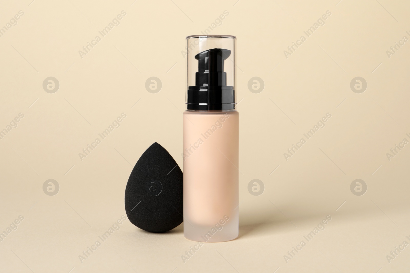 Photo of Bottle of skin foundation and sponge on beige background. Makeup product