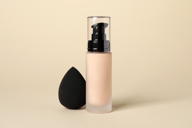 Bottle of skin foundation and sponge on beige background. Makeup product