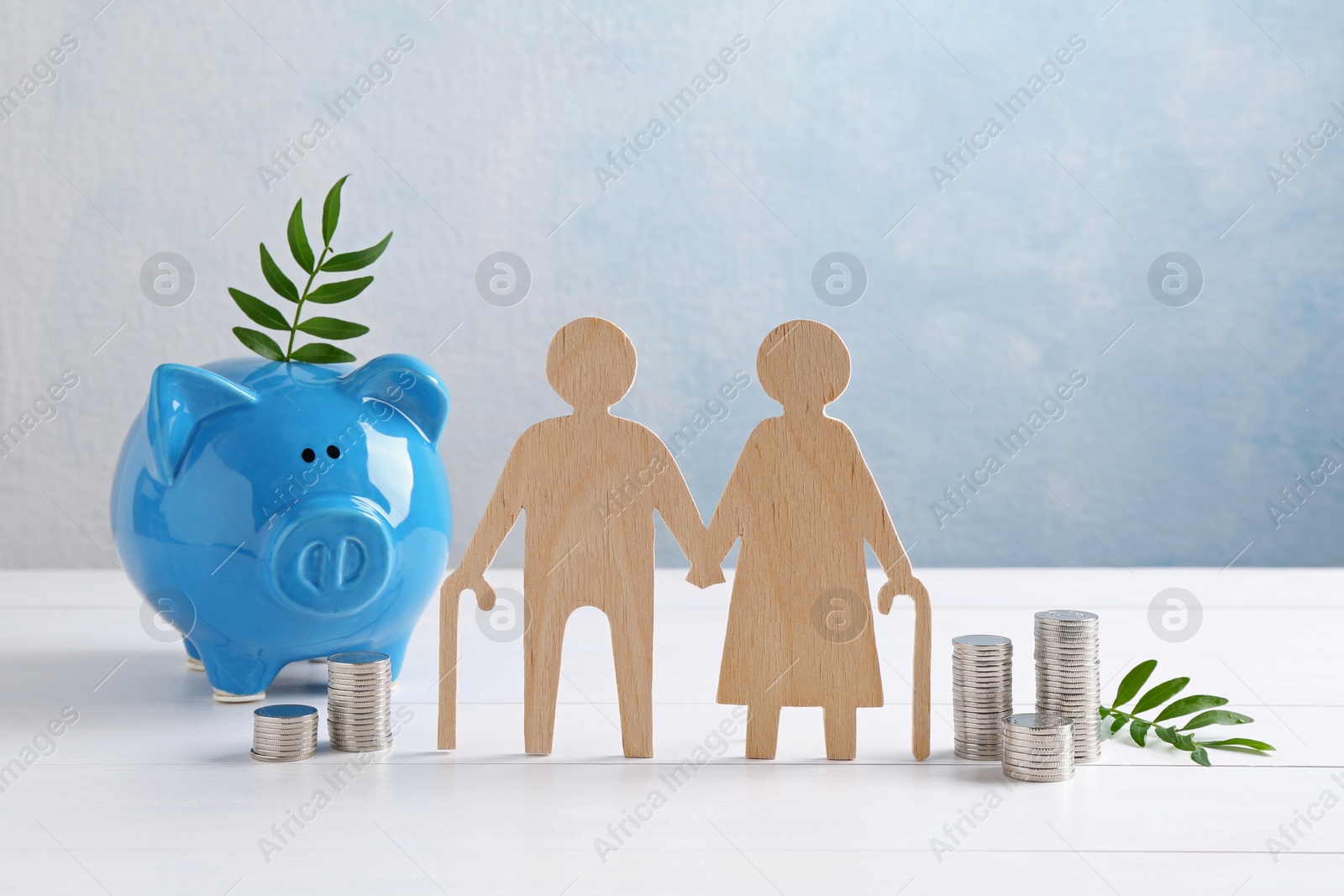 Photo of Pension savings. Figure of senior couple, stacked coins, piggy bank and green twigs on white wooden table