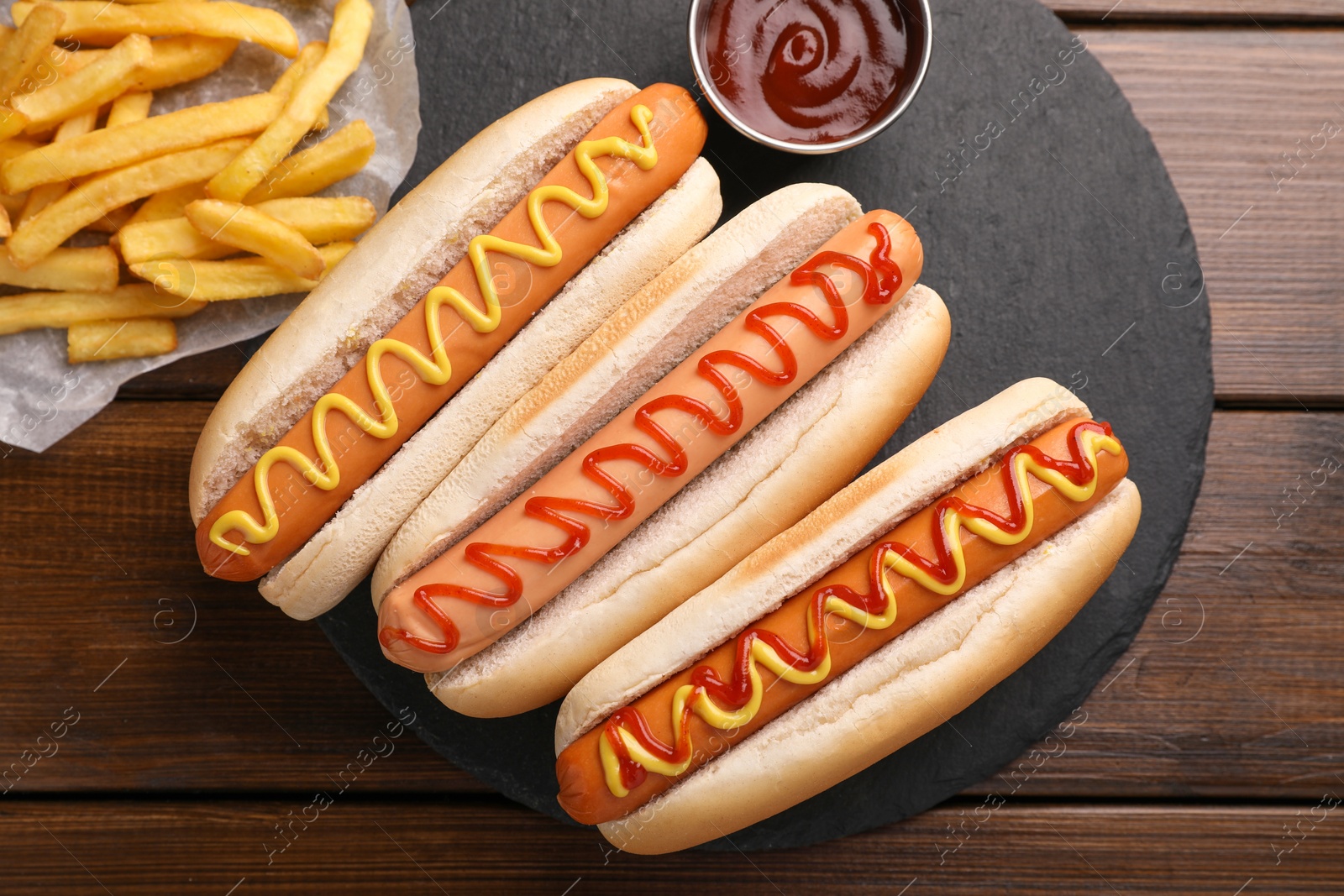 Photo of Delicious hot dogs with sauces and French fries on wooden table, top view