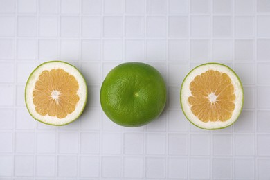 Whole and cut sweetie fruits on white tiled table, flat lay