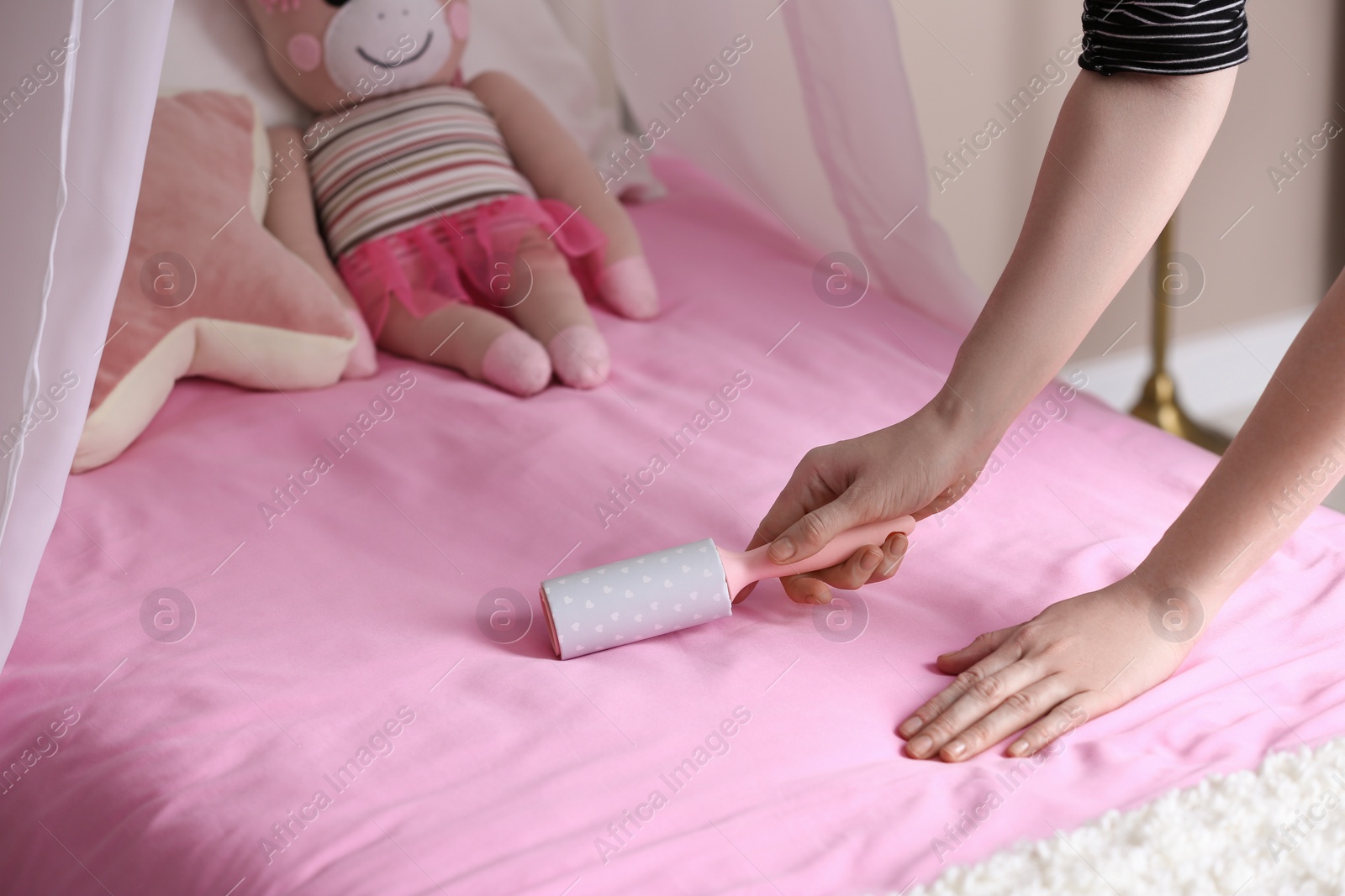 Photo of Woman cleaning bed with lint roller at home, closeup