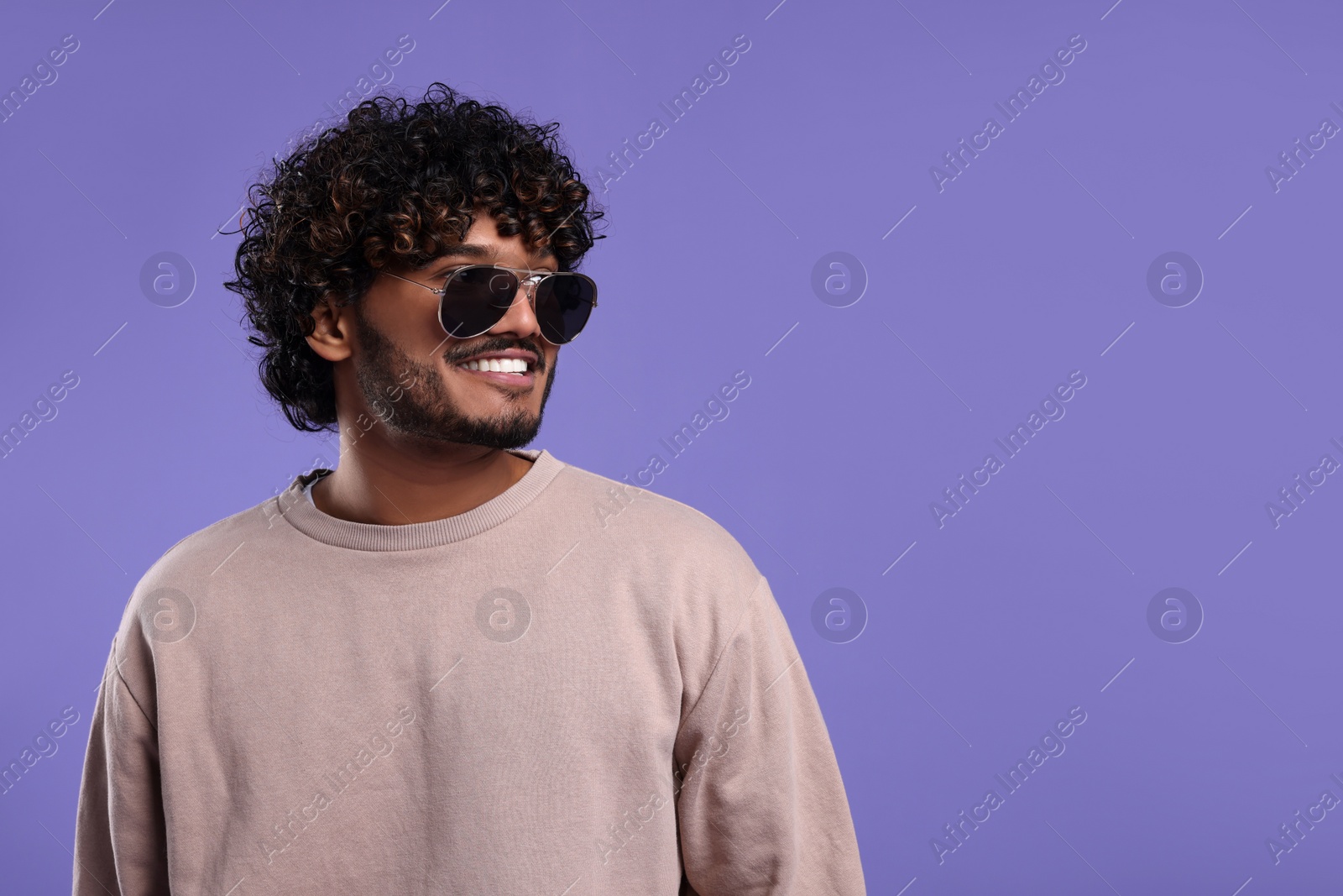 Photo of Handsome smiling man in sunglasses on violet background, space for text