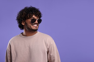 Handsome smiling man in sunglasses on violet background, space for text