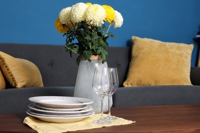 Photo of Vase with beautiful flowers, glasses and plates on wooden table in living room. Interior element