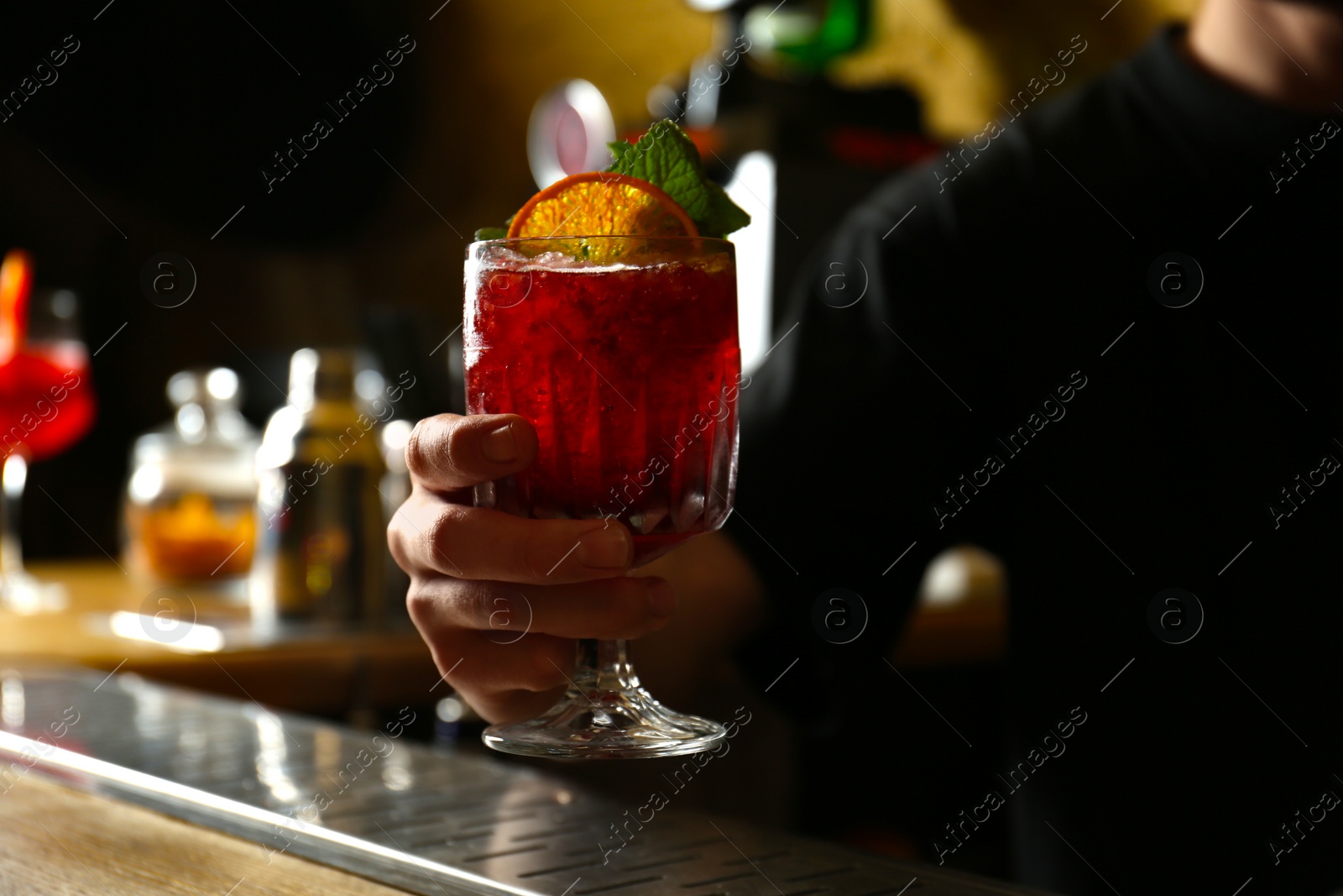 Photo of Bartender holding glass of fresh alcoholic cocktail in bar, closeup