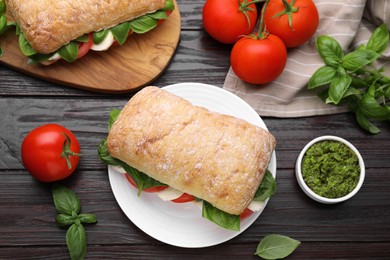 Delicious Caprese sandwiches with mozzarella, tomatoes, basil and pesto sauce on wooden table, flat lay