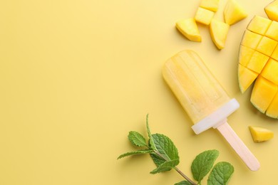 Photo of Tasty fruit ice pop with mango on light yellow background, flat lay. Space for text