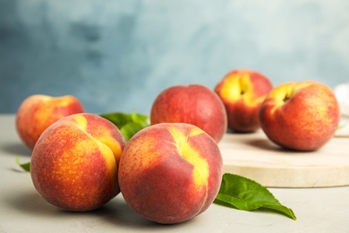 Photo of Tasty fresh peaches with leaves on grey table against blue background