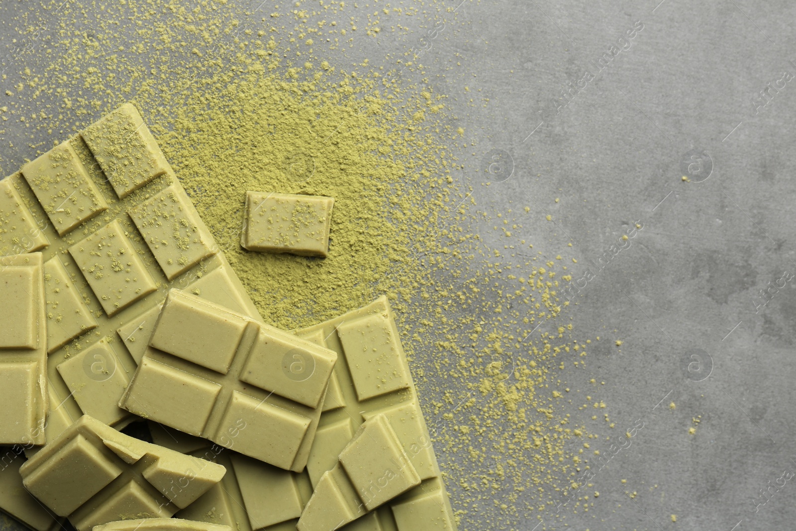 Photo of Pieces of tasty matcha chocolate bars and powder on grey textured table, top view. Space for text