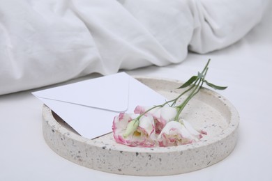 Tray with beautiful flowers and envelope on white bed