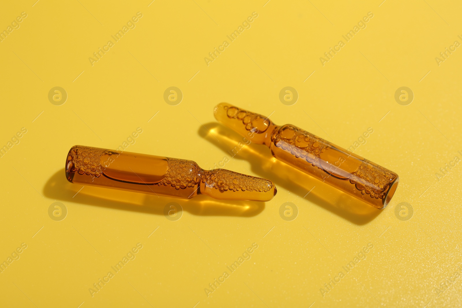 Photo of Glass ampoules with liquid on yellow background, closeup