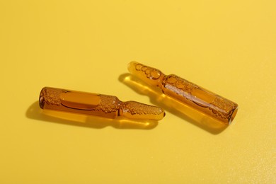 Photo of Glass ampoules with liquid on yellow background, closeup