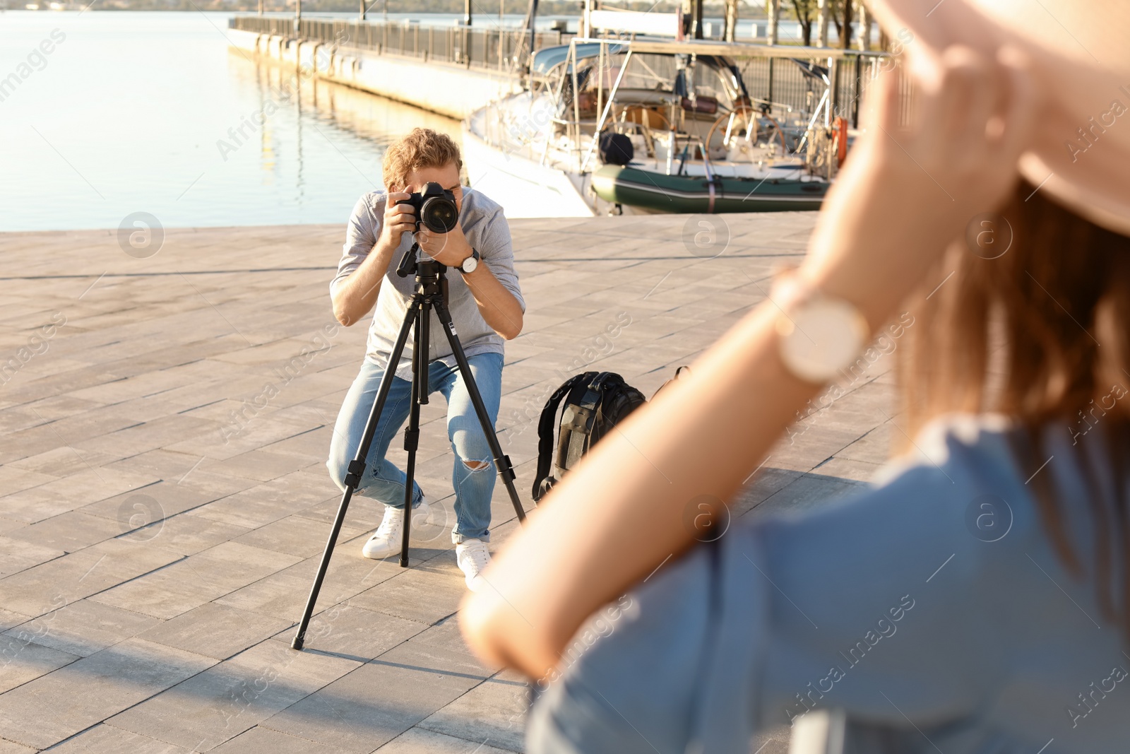 Photo of Male photographer taking photo of young woman with professional camera at pier