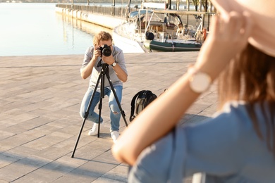 Photo of Male photographer taking photo of young woman with professional camera at pier