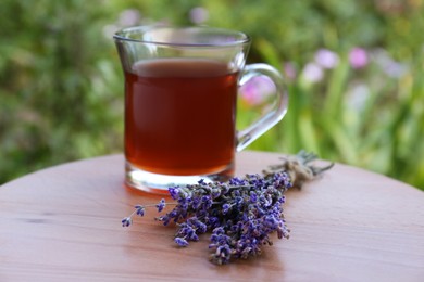 Photo of Beautiful lavender flowers and cup of aromatic tea on wooden table, closeup