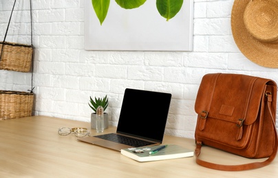 Photo of Stylish workplace with modern laptop on table near brick wall. Fashion blogger