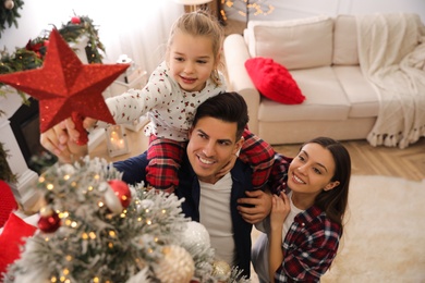 Family decorating Christmas tree with star topper indoors