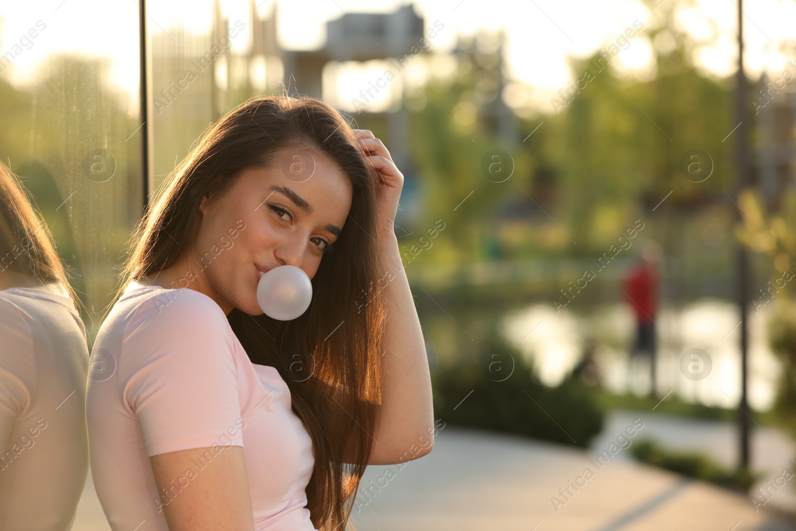 Photo of Beautiful young woman blowing bubble gum outdoors. Space for text