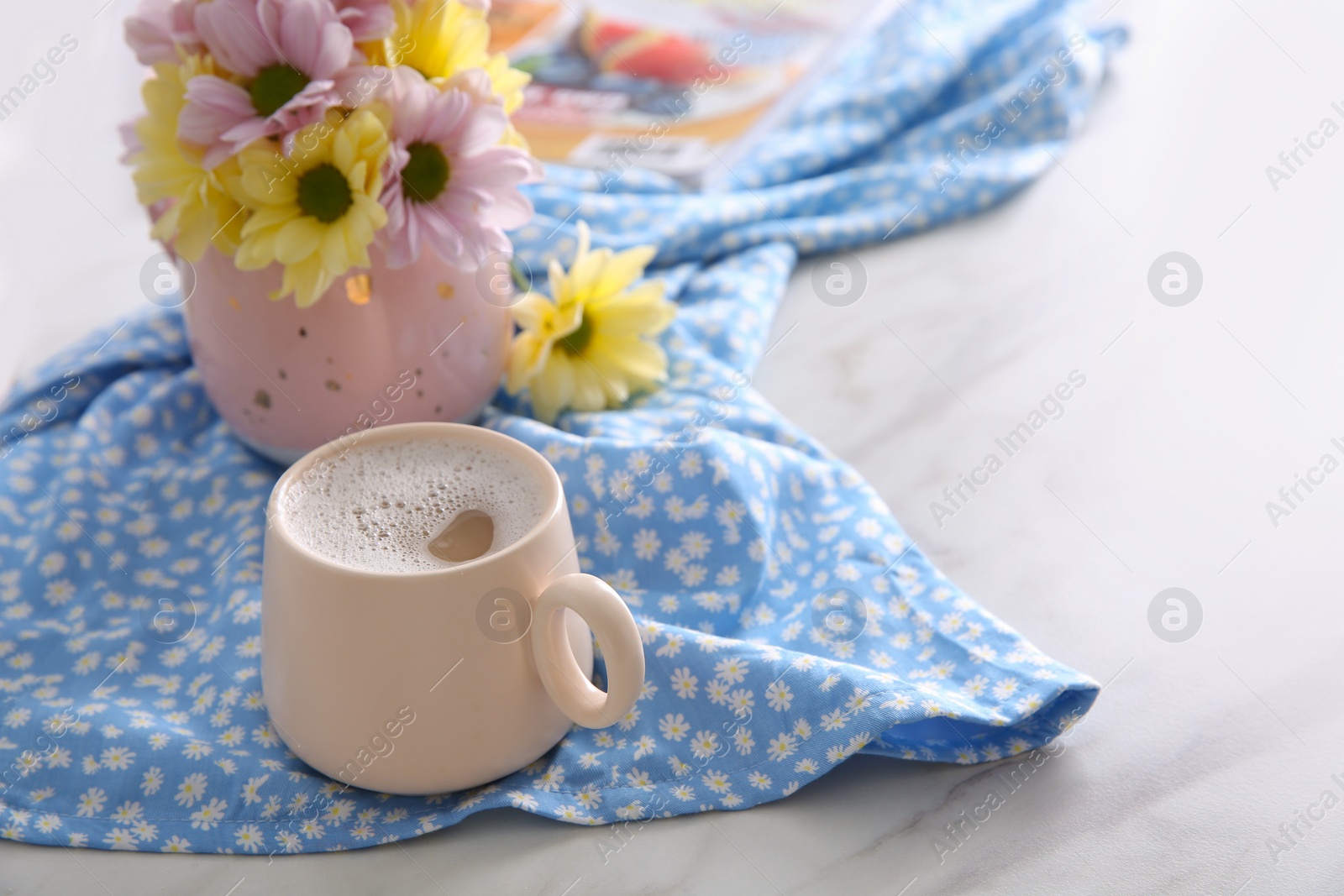 Photo of Cup of fresh coffee, beautiful bouquet and light blue printed cloth on white marble table, space for text. Good morning