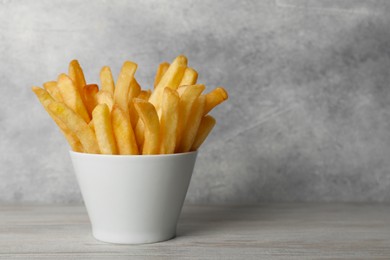 Photo of Delicious fresh french fries in bowl on light gray wooden table, closeup. Space for text