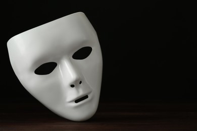 Photo of White theatre mask on wooden table against black background, space for text