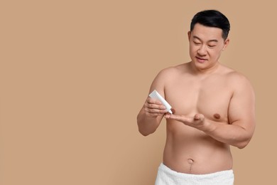 Handsome man applying body cream onto his hand on light brown background. Space for text