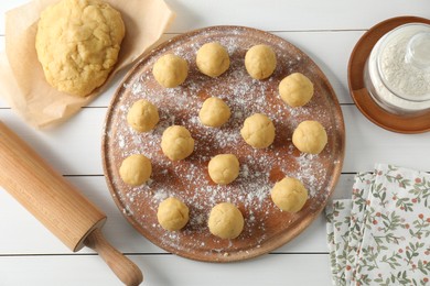 Photo of Shortcrust pastry. Raw dough balls, flour and rolling pin on white wooden table, flat lay
