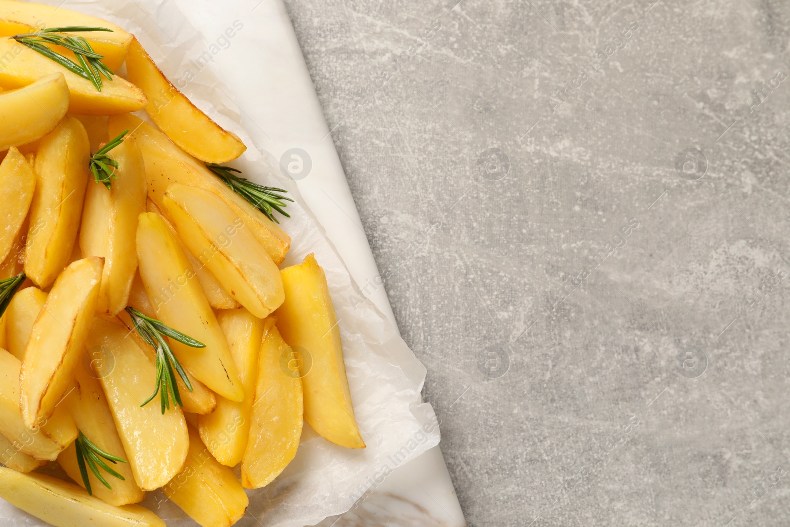 Photo of Tasty baked potato wedges and rosemary on grey table, top view. Space for text