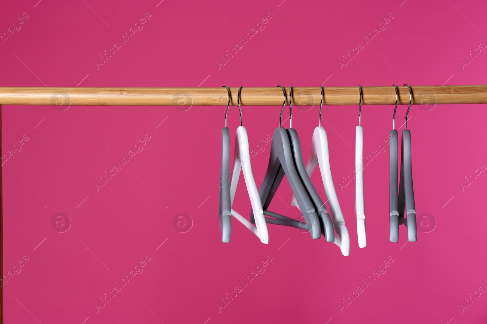 Photo of Wooden rack with clothes hangers on color background, space for text