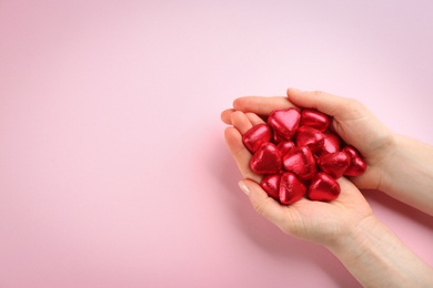 Photo of Woman holding heart shaped chocolate candies on pink background, top view. Space for text